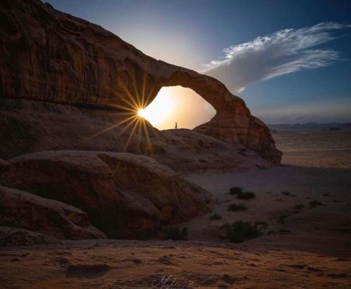a person standing under an arch in the desert at غرووب وادي رم in Wadi Rum
