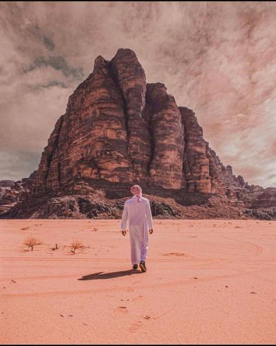 a man walking in the desert in front of a mountain at غرووب وادي رم in Wadi Rum