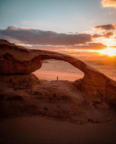a person standing on a beach under an arch in the sunset at غرووب وادي رم in Wadi Rum