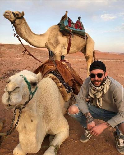 a man kneeling next to a camel in the desert at غرووب وادي رم in Wadi Rum