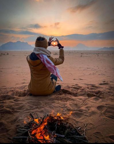 a person sitting next to a fire on the beach at غرووب وادي رم in Wadi Rum