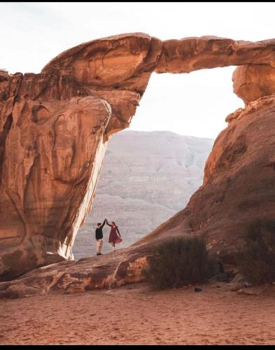 two people standing under a rock in the desert at غرووب وادي رم in Wadi Rum