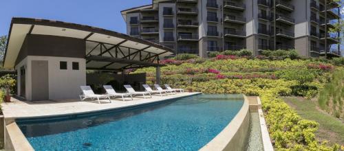 a swimming pool with chairs and a building at Roble Sabana 105 Luxury Apartment - Reserva Conchal in Playa Conchal