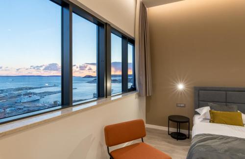 Seascape Luxury Rooms في سبليت: غرفة نوم بنوافذ كبيرة وسرير وكرسي
