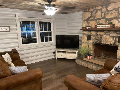 a living room with a television and a stone fireplace at Creekside Hideaway - Real Log Cabin w/Great Location in Pigeon Forge
