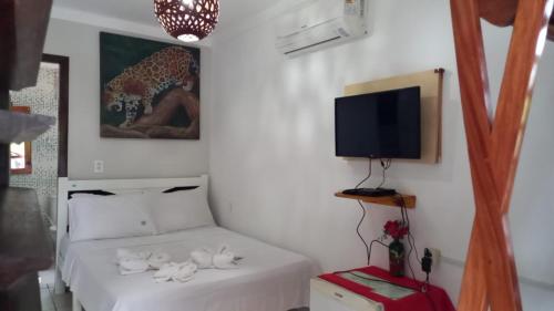 um quarto com uma cama com lençóis brancos e uma televisão em Pousada Numei de Jeri em Jericoacoara
