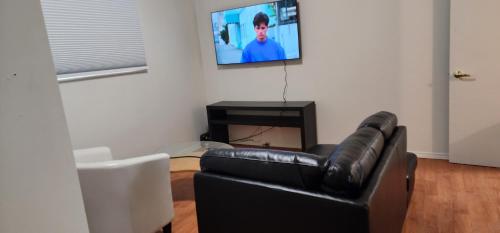 a living room with a black leather couch and a flat screen tv at ChessKings Guest House - Unit 1 in Winnipeg