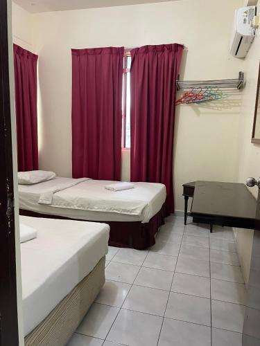 a room with two beds and a window with red curtains at KUHARA COURT APARTMENT SUITE in Tawau