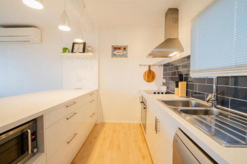a kitchen with white cabinets and a sink and a window at Aldinga Beach Break - C21 SouthCoast Holidays in Aldinga Beach