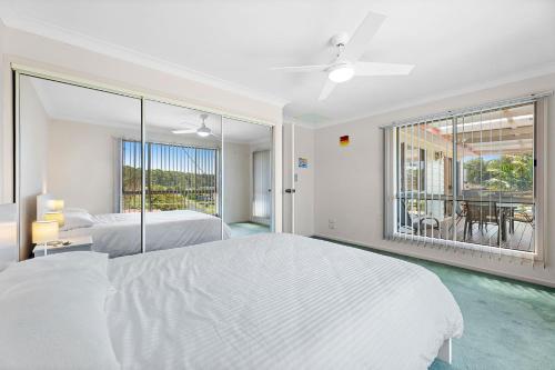 a white bedroom with two beds and a large window at 28 Nioka Street in Dalmeny