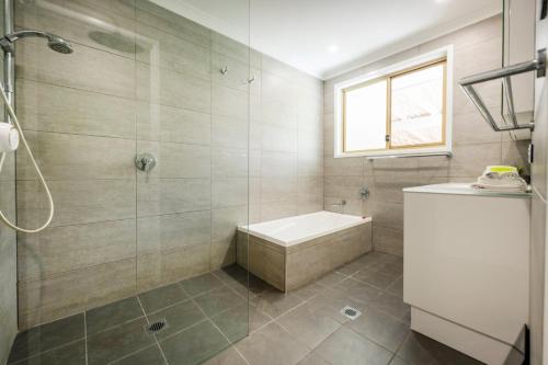 a bathroom with a shower and a tub and a sink at Kailani Beach House - LJHooker Yamba in Yamba