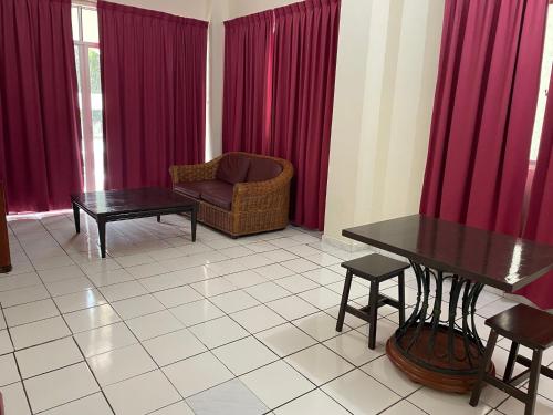 a living room with red curtains and a table and a chair at KUHARA COURT APARTMENT SUITE in Tawau