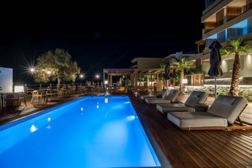 einen Pool in der Nacht mit Liegestühlen und Tischen in der Unterkunft AKASHA Beach Hotel & Spa in Hersonissos