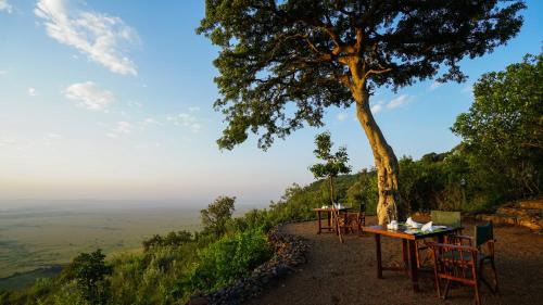 a table and chairs sitting on a hill with a tree at Mara Elatia Camp in Masai Mara