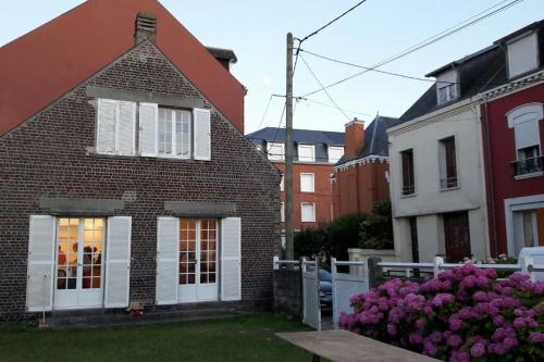 une maison en briques avec des fleurs violettes dans la cour dans l'établissement Les Picantins de Cayeux sur mer, à Cayeux-sur-Mer