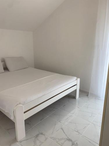 a white bed in a room with a tiled floor at Apartman Jaca in Mrčevac
