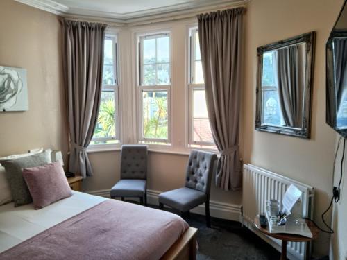een slaapkamer met een bed en 2 stoelen en ramen bij Kingsholm Guest House in Torquay