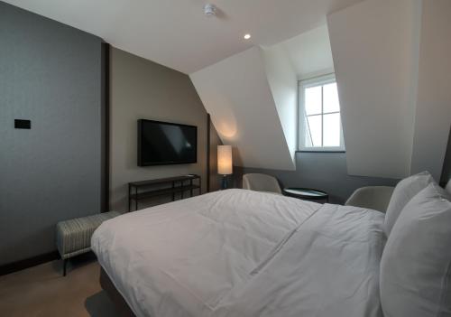 a bedroom with a white bed and a television at Hotel de Schelde in Cadzand-Bad