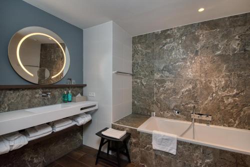 a bathroom with a tub and a sink and a mirror at Hotel de Schelde in Cadzand-Bad