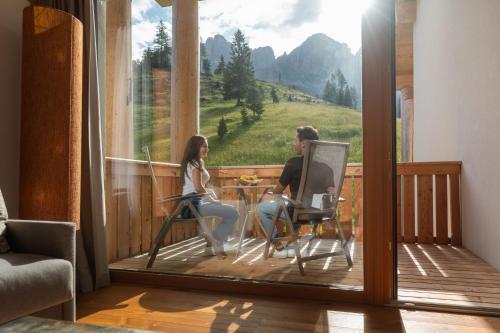 two women sitting at a table on a balcony at Moseralm Dolomiti Spa Resort in Nova Levante