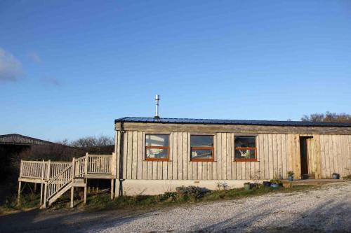 a small wooden house with a porch on a street at Spacious cabin on isolated farm with sea view in Bude