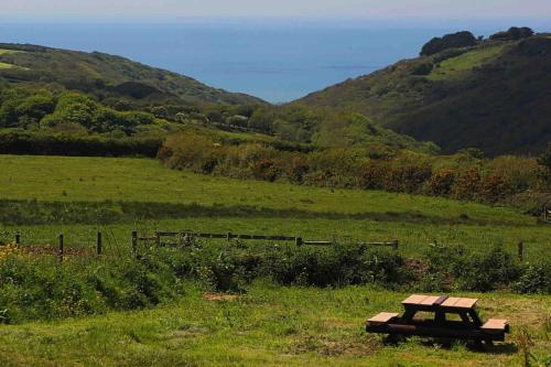 a picnic table in a field with hills in the background at Spacious cabin on isolated farm with sea view in Bude