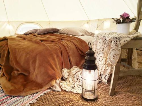 a bed with a blanket and a lantern on the floor at Karkausmäki Glamping in Kinnula