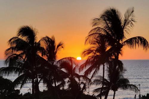 a sunset with palm trees on the beach at Island Surf 601A in Kihei