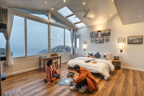 two people sitting on the floor in a bedroom with a bed at Zostel Homes Shimla in Shimla