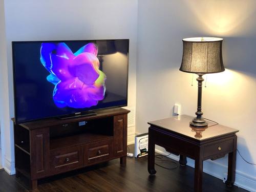 a flat screen tv sitting on a wooden stand next to a lamp at Niagara sleeps 6 Cozy 3bed3bath Near Falls in Thorold