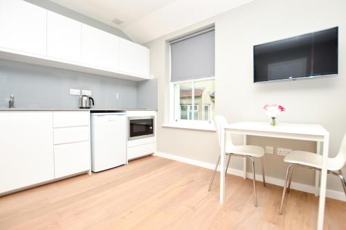 uma cozinha com armários brancos e uma mesa e cadeiras em Fitzroy Serviced Apartments by Concept Apartments em Londres