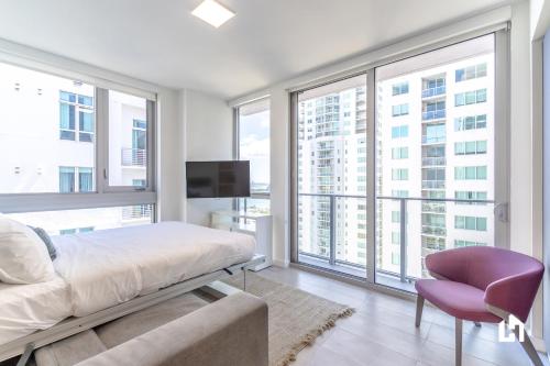 a bedroom with a bed and a chair and large windows at Downtown Miami Condos by Lua Host in Miami