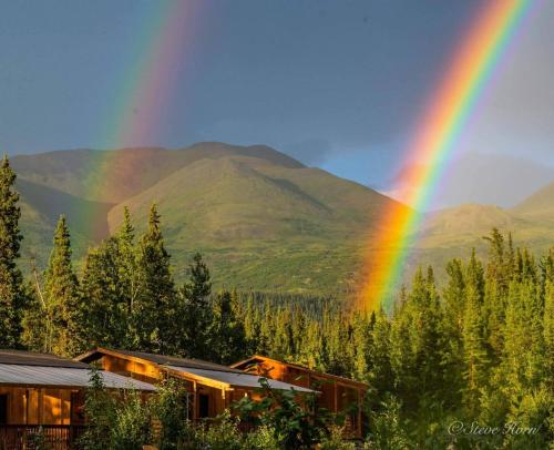 a rainbow over a house with mountains in the background at McKinley Creekside Cabins in McKinley Park