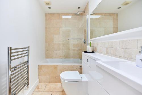 a white bathroom with a toilet and a tub at The Elmbridge Getaway - Glamorous 2BDR with Garden in London