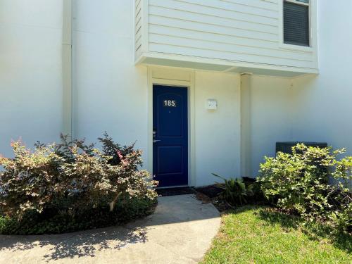 een wit huis met een blauwe deur en wat struiken bij Villas by The Sea Deluxe Two Bedroom Apartment in Jekyll Island