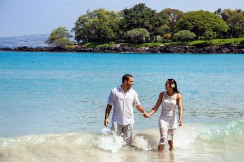 a man and woman walking in the water on the beach at Mauna Kea Beach Hotel, Autograph Collection in Hapuna Beach