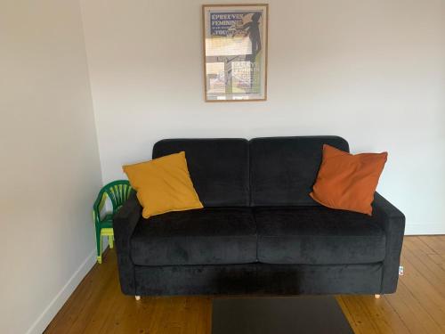 - un canapé noir avec deux oreillers orange dans l'établissement Le Touquet Paris Plage - Le Vent des Anges ., à Le Touquet-Paris-Plage