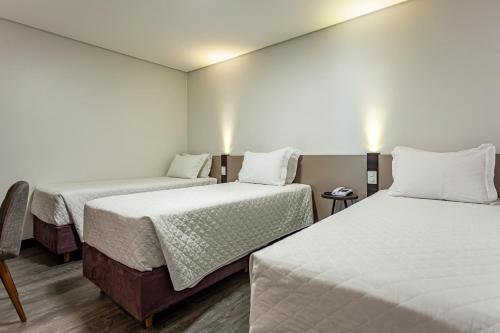 two beds in a room with white walls and wooden floors at Travel Inn Hotels Caxias do Sul in Caxias do Sul