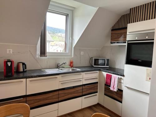 een keuken met witte kasten, een wastafel en een raam bij Studio cosy au centre de Couvet in Couvet