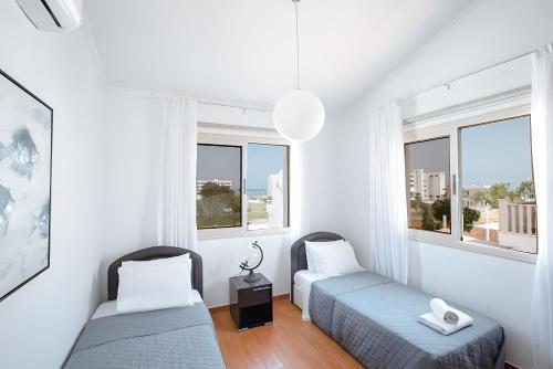 two beds in a white room with windows at Blue Crystal Seaview in Protaras
