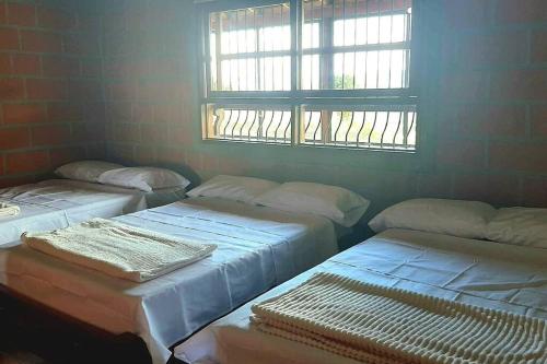 three beds in a room with a window at Casa de Campo vía El Peñol Guatapé in Marinilla