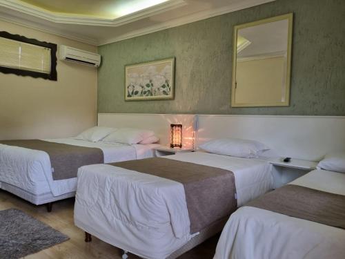a room with three beds and a mirror on the wall at Pousada Caliandra Da Serra in Canela