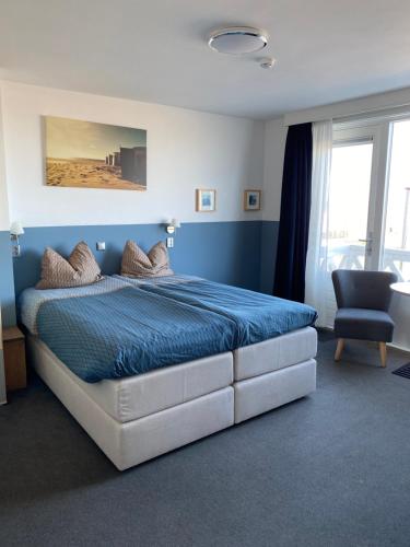 a bedroom with a bed with a blue comforter and a chair at Bed&Breakfast aan Strand in Katwijk aan Zee