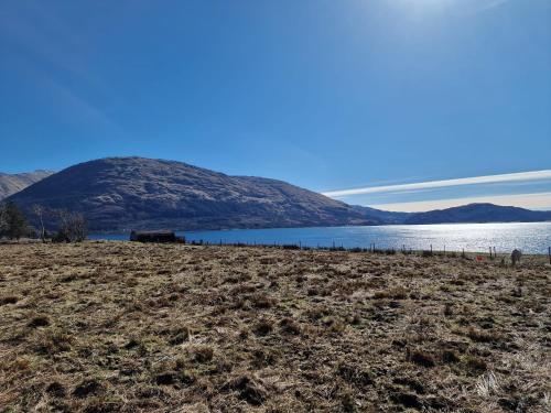 a field next to a body of water with a mountain at Dalrigh Pod in Onich