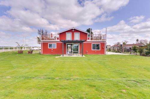 a red house in a field with a green yard at Rustic California Vacation Rental with Rooftop Patio in Tulare