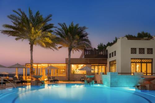 a swimming pool in front of a house with palm trees at Ajman Saray, a Luxury Collection Resort, Ajman in Ajman