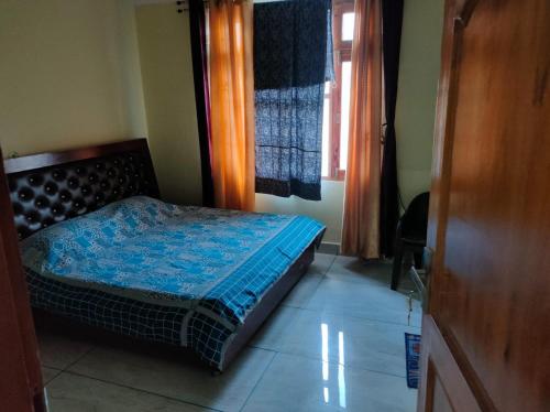 a bedroom with a bed with a blue comforter and a window at Mahamaya Homestay 4 in Mandi