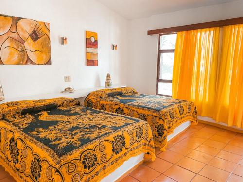 2 łóżka w pokoju z żółtymi zasłonami i oknem w obiekcie El Palmar Beach Tennis Resort w mieście San Patricio Melaque