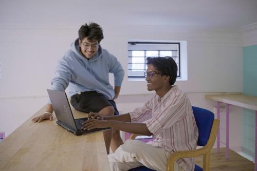two men sitting on a table with a laptop at Rahees Bi Roambay - Backpacker Hostel in Mysore