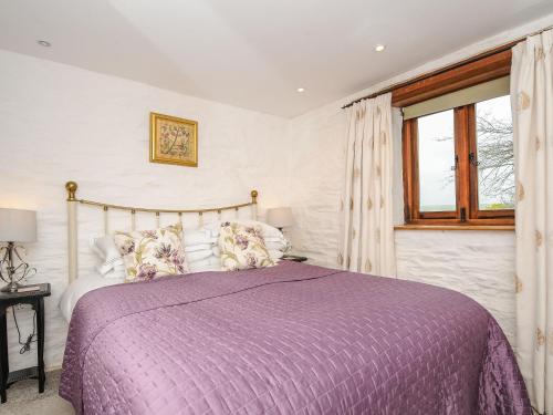 ein Schlafzimmer mit einem Bett mit einer lila Bettdecke und einem Fenster in der Unterkunft Swallow Barn in Saint Kew